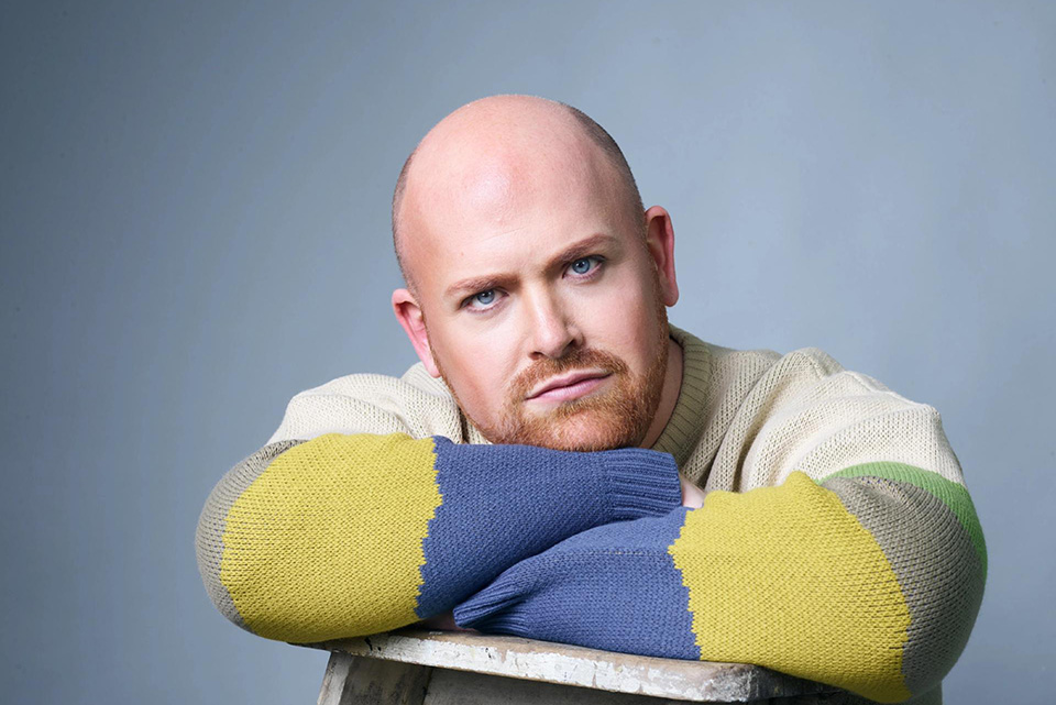 A man dressed in a blue and yellow jumper looking into the camera